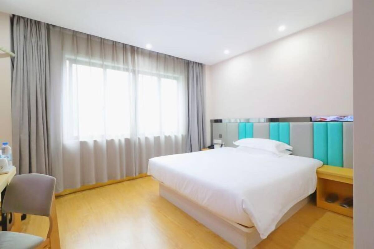 Quarto de hotel com cama, escrivaninha, cadeira e janela com cortinas.