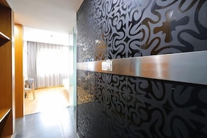 Eine moderne Hotellobby mit Wandverkleidung, einer Rezeption und Blick auf einen Raum mit Bett und Vorhängen.