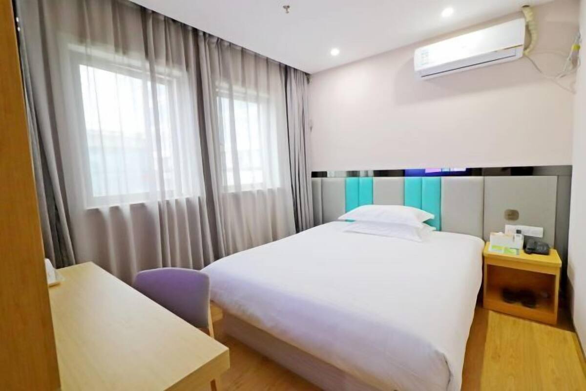 Quarto de hotel com cama, escrivaninha, cadeira, mesa de cabeceira e ar condicionado.