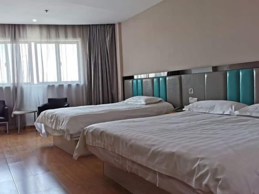 A hotel room with two beds, a chair, a small table, and a window with curtains.