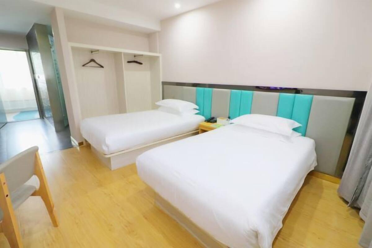 Quarto de hotel com duas camas de solteiro, uma cadeira de madeira e um guarda-roupa com cabides.