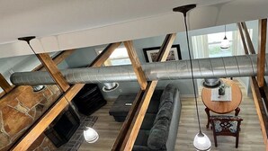 A loft-style room with exposed wooden beams, a stone fireplace, a large window, and a cozy seating area with a sofa and a small table. - Cabin B Unit 3, Cast Your Cares Away Here! (Lebanon)