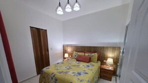 Quarto com cama, cabeceira de madeira, mesas de cabeceira e uma porta.