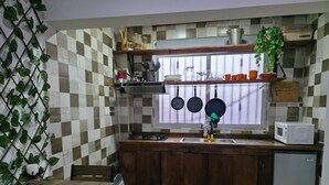 Uma cozinha compacta com armários de madeira, micro-ondas embutido e janela com panelas penduradas.
