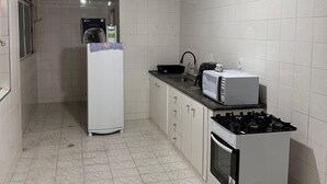 A kitchen with white tiled walls, a refrigerator, a microwave, a stove, and a sink. - A 4 Minutos da Basílica! Apartamento Para Famílias (Aparecida)