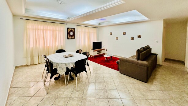 A living room with a dining table, a sofa, a TV, and a red carpet. - A 4 Minutos da Basílica! Apartamento Para Famílias (Aparecida)