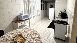 A compact kitchen with a microwave, refrigerator, and stove. A dining table with a patterned tablecloth is in the foreground. - A 4 Minutos da Basílica! Apartamento Para Famílias (Aparecida)