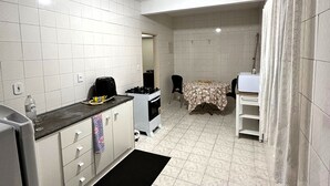 A compact kitchen with white tiled walls, a black countertop, and a small dining area with a table and chairs. - A 4 Minutos da Basílica! Apartamento Para Famílias (Aparecida)