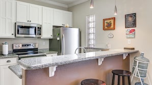 A kitchen with white cabinets, stainless steel appliances, granite countertops, and a bar area with stools. - South Padre Island: Pool Access, 1 Block to Beach! (South Padre Island)