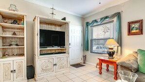 A living room with a television, wooden cabinet, and a green couch. - South Padre Island: Pool Access, 1 Block to Beach! (South Padre Island)
