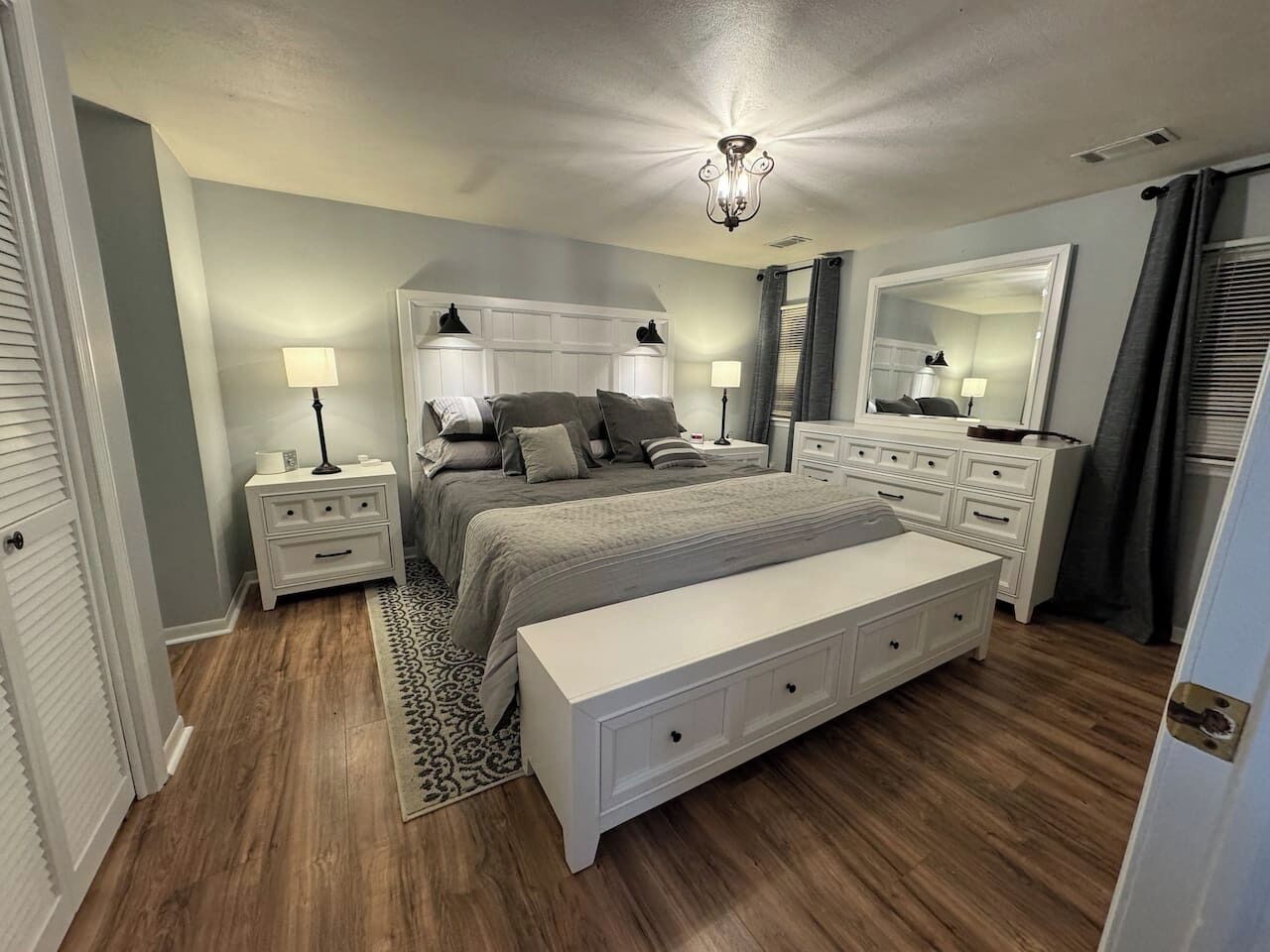 A bedroom with a bed, bedside tables, a bench, a dresser, and a mirror.