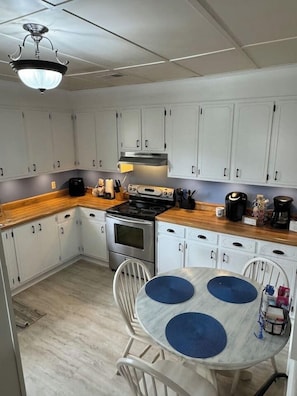 A kitchen with white cabinets, a stove, a sink, and a dining table with blue placemats. - Pool, ZERO cleaning fee, free covered parking, Tempur-Pedic KING bed. (Beech Island)