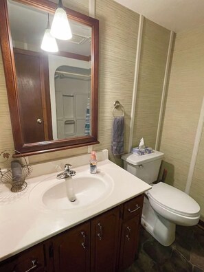 Baño con lavamanos blanco, espejo, aro para toallas y retrete.