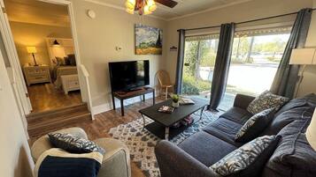 A living room with a sofa, a coffee table, a TV, a ceiling fan, and a painting on the wall.