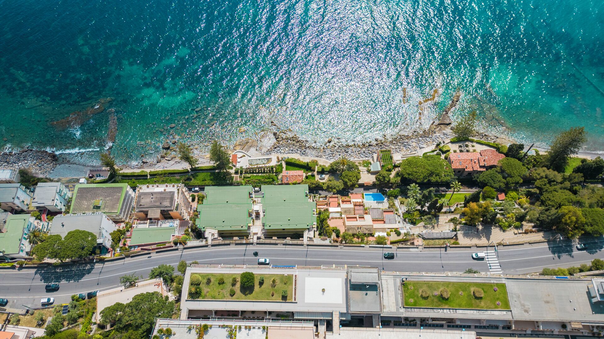 An aerial view of a coastal residential area with houses, a road, and a beach.