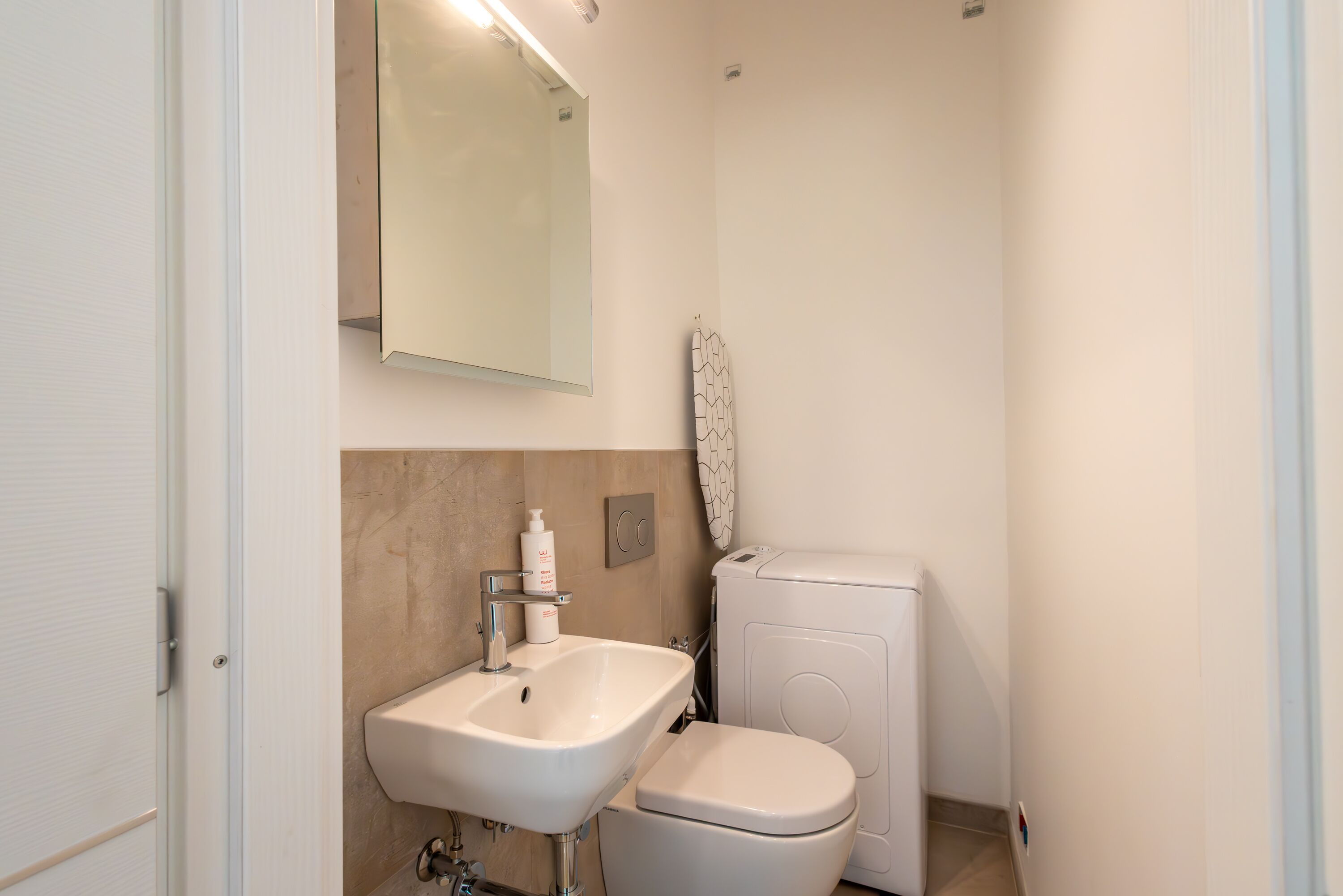 A small, modern bathroom with a white sink, toilet, and a mirror above the sink.