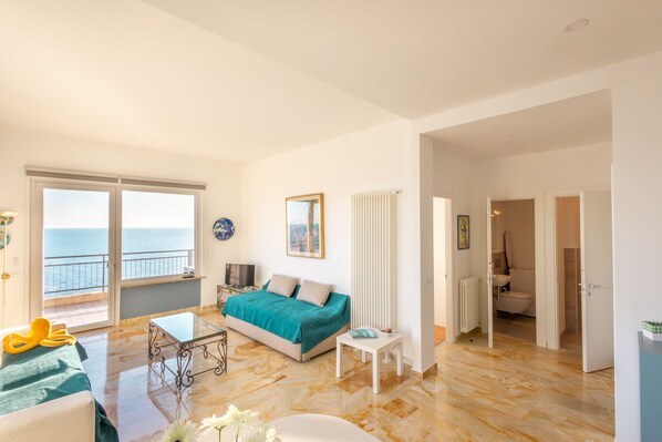 Une chambre spacieuse avec un grand lit, une table en verre et une vue sur la mer, accessible par une porte coulissante.