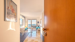 A hallway leading to a dining area with a table and chairs, a sofa, and a window with blinds. - Sky & Sea Apartment by Wonderful Italy (Ospedaletti)
