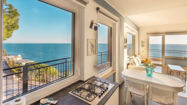 A modern kitchen with a gas stove, large windows overlooking the sea, and a dining area with a white table and chairs. - Sky & Sea Apartment by Wonderful Italy (Ospedaletti)