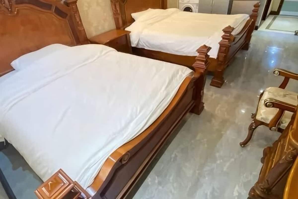 Zwei hölzerne Betten mit weißer Bettwäsche, ein Holzstuhl und ein Marmorboden.