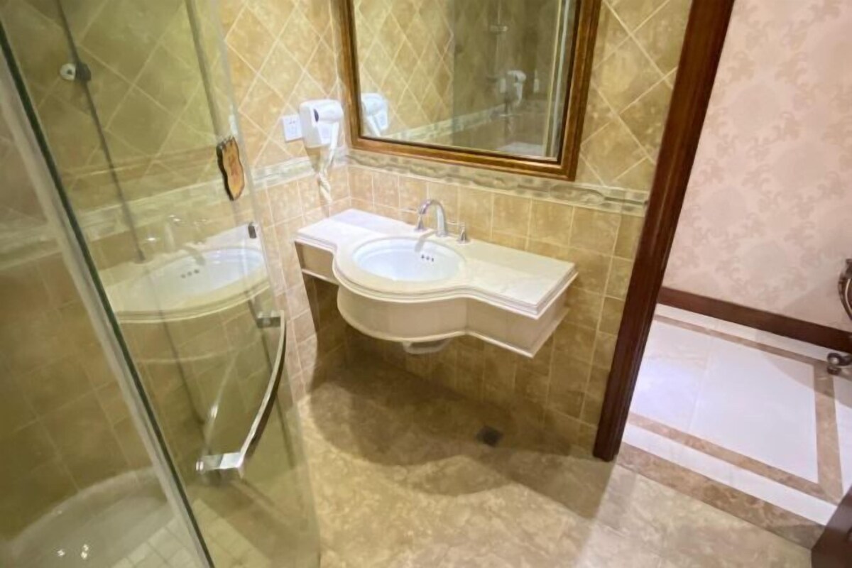 Een badkamer met een douchecabine van glas, een wastafel met spiegel en een betegelde vloer.