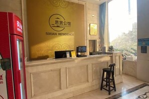 A reception desk with a sign reading 'SIXIAN RESIDENCE' and a small screen. There is a window with a view of trees and a red machine to the left. - Haosheng E-sports Hotel (Shanghai)