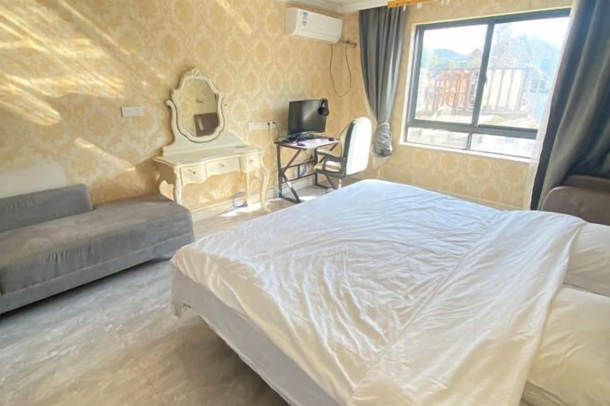 Ein Hotelzimmer mit Bett, Schreibtisch, Sessel, Fernseher und einem fenster mit Vorhängen.