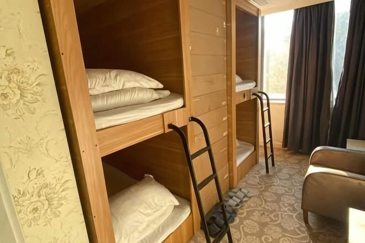 Ein Zimmer mit Etagenbetten, einer Leiter, einem Stuhl und einem Fenster mit Vorhängen.
