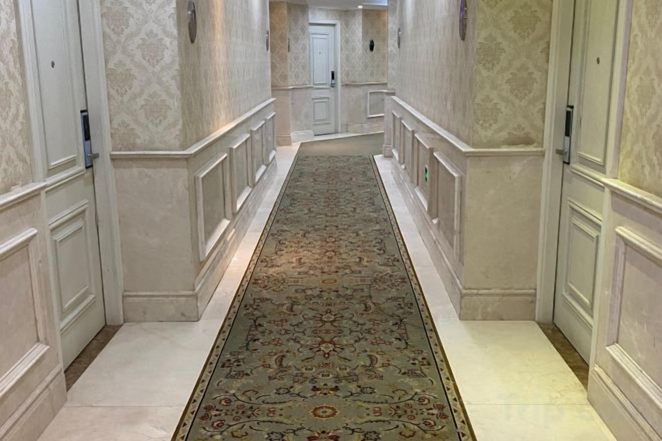 A hallway with a patterned carpet, white walls, and a door at the end.