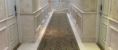 A hallway with a patterned carpet, white walls, and a door at the end.