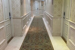 Un couloir avec un tapis à motifs, des murs blancs et une porte au fond.