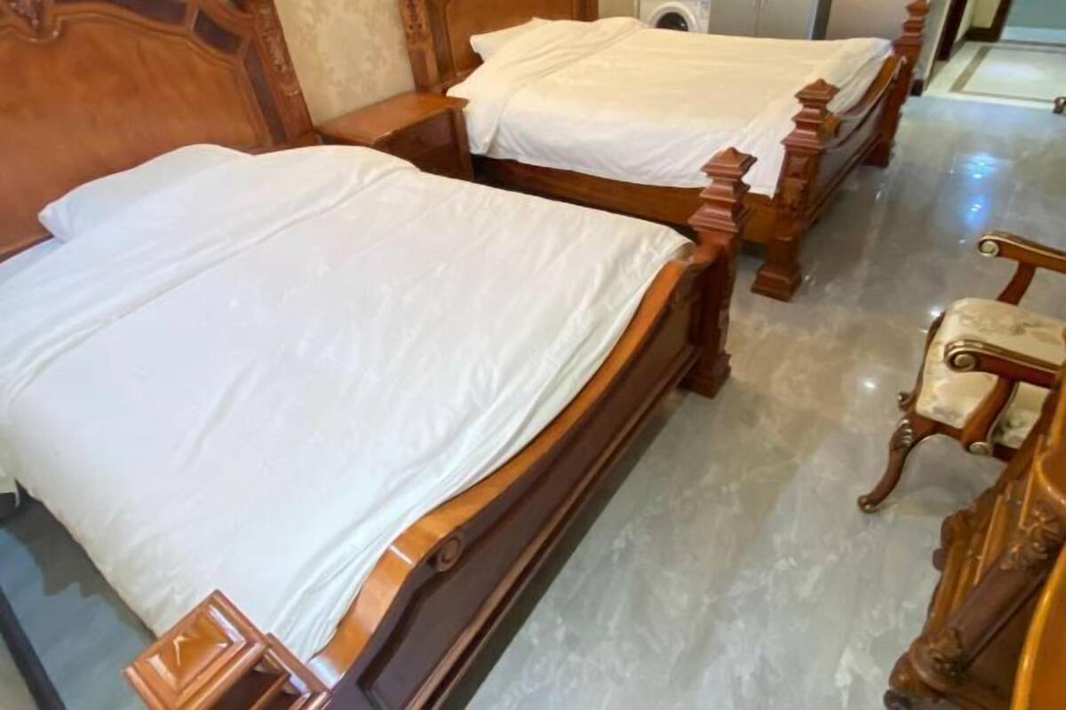 Ein Hotelzimmer mit zwei hölzernen Betten, einem Nachttisch aus Holz, einem Sessel und einem Marmorboden.