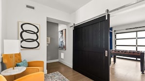 A modern living room with a sofa, artwork, and a sliding door leading to a game room. - Centennial Quarters: Holiday House near Vandy! (Nashville)