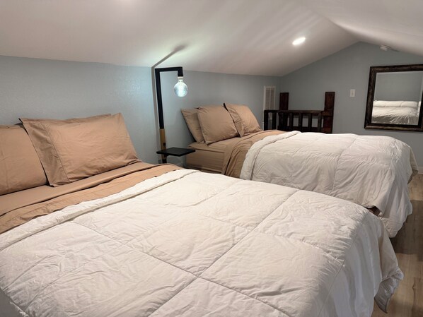 Ein Zimmer mit zwei Betten, einem Nachttisch, einer Lampe, einem Spiegel und Holzboden.