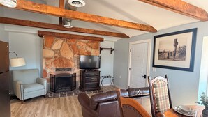 Ein Wohnzimmer mit Kamin aus Stein, Ledersofa, Esstisch aus Holz und einem an der Wand befestigten Fernseher.