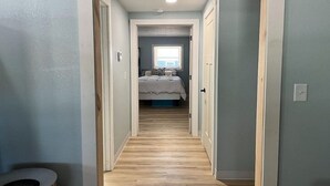 Ein schmaler Flur führt zu einem Schlafzimmer mit Bett und Fenster.