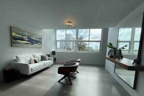 Una sala de estar moderna con un sofá blanco, una mesa de centro y un ventanal con vistas a la ciudad.