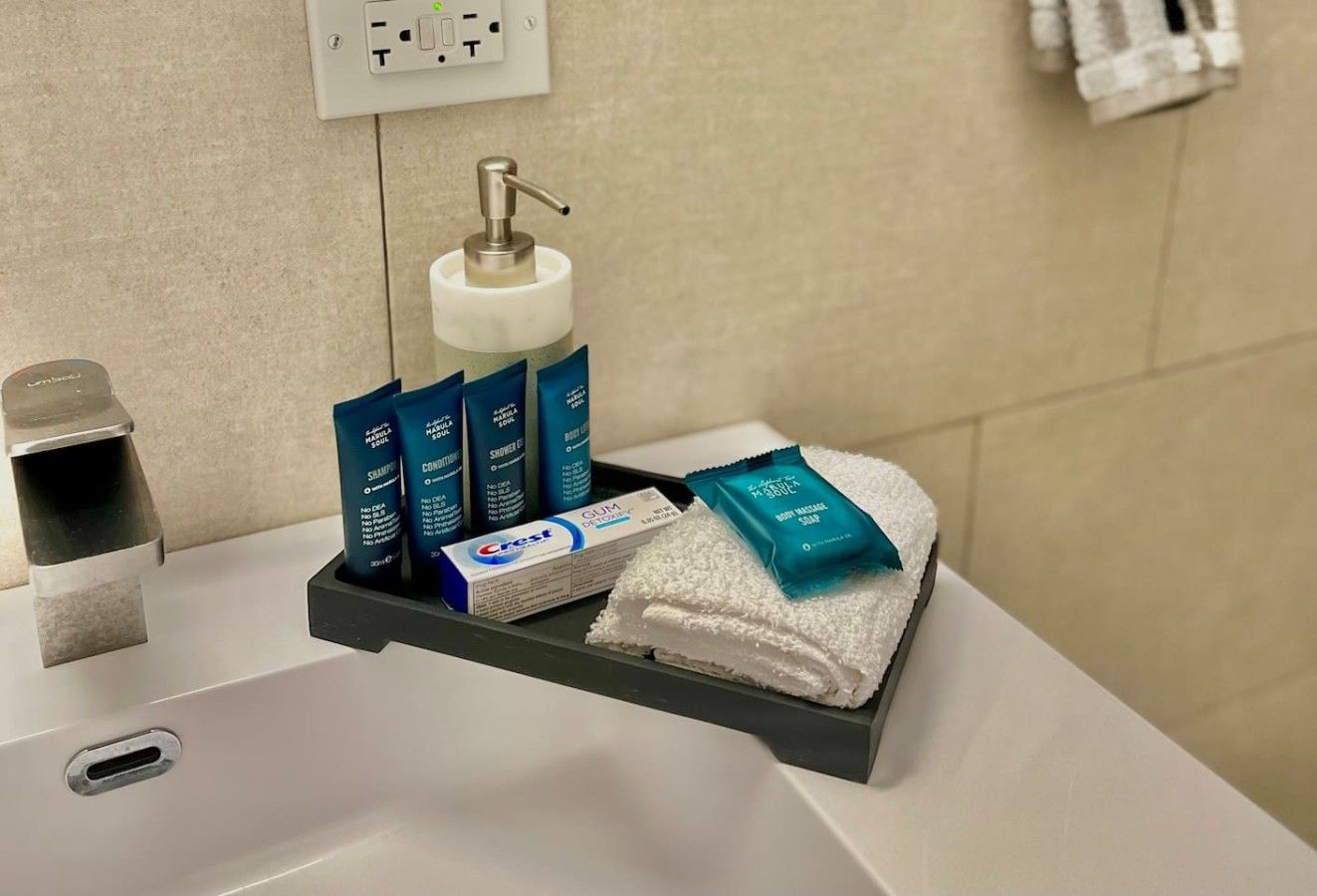 Un lavandino in bagno con un dispenser di sapone, shampoo, balsamo e un asciugamano su un vassoio.
