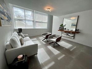 Een moderne woonkamer met een witte bank, twee fauteuils, een salontafel en een groot raam dat voor natuurlijk licht zorgt.