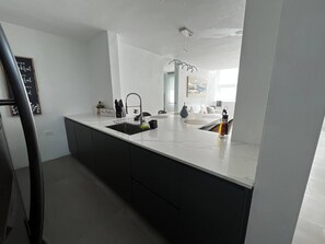 Una cocina moderna con encimera blanca, armarios negros e iluminación colgante.