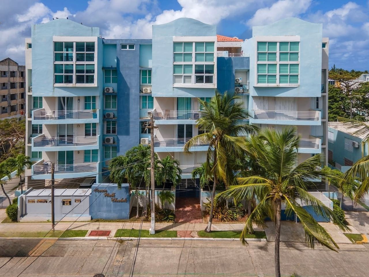 Un hotel de varios pisos con balcones, palmeras y un cielo despejado.