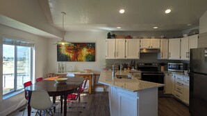 A modern kitchen with white cabinets, granite countertops, and stainless steel appliances. There is a dining area with a wooden table and chairs, and a large window providing a view of the outdoors. - Nature's Playground for All Seasons. Near World Class Ski Resorts & Golf Courses (Sandy)