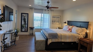 A bedroom with a bed, bedside tables, a ceiling fan, a window with blinds, a TV mounted on the wall, and a potted plant. - Nature's Playground for All Seasons. Near World Class Ski Resorts & Golf Courses (Sandy)