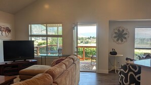 A spacious living room with a high ceiling, a ceiling fan, a large window, a television, and a view of the outdoors. - Nature's Playground for All Seasons. Near World Class Ski Resorts & Golf Courses (Sandy)
