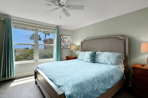 A bedroom with a bed, a nightstand, a ceiling fan, a window with curtains, and a wall with a framed quote. - Coquina A104 Ground floor walk out unit. Direct Ocean View! (Saint Augustine Beach Florida)