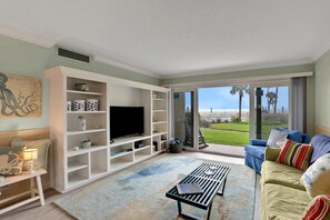 A living room with a television, a sofa, a coffee table, and a view of the outdoors. - Coquina A104 Ground floor walk out unit. Direct Ocean View! (Saint Augustine Beach Florida)