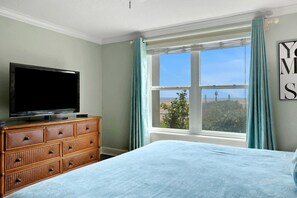 Un dormitorio con cama, cómoda, televisor y ventana con cortinas.