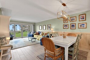 A dining area with a table and chairs, a sofa set, and a view through a glass door to the outdoors. - Coquina A104 Ground floor walk out unit. Direct Ocean View! (Saint Augustine Beach Florida)