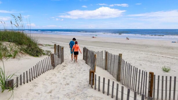 A sandy beach with a wooden fence leading to the water.