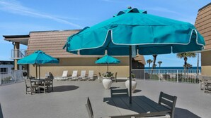 An outdoor seating area with tables and chairs, umbrellas, and a view of the ocean.